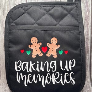 May include: Black quilted oven mitt with a white design of two gingerbread men and the text "baking up memories".