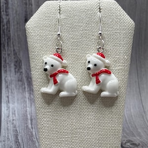 May include: A pair of silver dangle earrings featuring white polar bear charms wearing red Santa hats and red scarves.