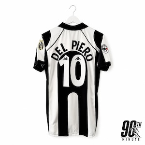 May include: A black and white striped soccer jersey featuring the name DEL PIERO and the number 10 printed in black on the back. The shirt includes a black collar, short sleeves with team logos on the shoulders, and the Kappa brand logo above the number.