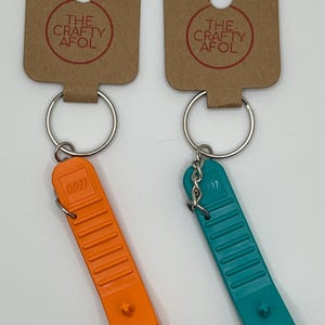 May include: Two LEGO brick keychain charms, one orange and one teal, with a silver key ring and a brown tag that reads "The Crafty AFOL".