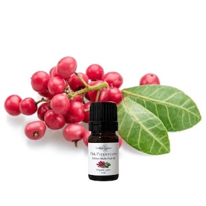 Könnte beinhalten: Eine kleine braune Flasche ätherischen Öls mit schwarzem Verschluss befindet sich neben einer Ansammlung leuchtend rosa Pfefferkörner und grünen Blättern. Das Etikett lautet "Pink Peppercorn Schinus Molle Fruit Oil" und "Organic, pure 5 ml."