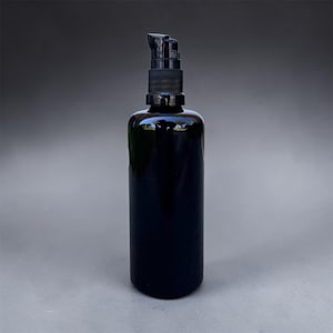 Puede incluir: Una botella de vidrio negro con un dispensador de bomba. La botella cilíndrica tiene una base redondeada y una parte superior de bomba negra. El vidrio oscuro refleja la luz. Producto para el cuidado de la piel o belleza, aprox. 100 ml.
