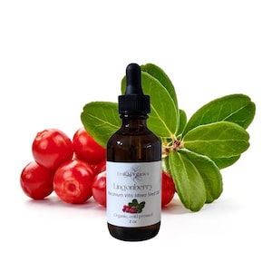 Pode incluir: Uma garrafa de vidro castanho com conta-gotas preto, rotulada "Lingonberry Vaccinium Vitis Idaea Seed Oil". A garrafa está ao lado de um grupo de mirtilos vermelhos e folhas verdes. O rótulo indica que o óleo é orgânico e prensado a frio, e contém 59 ml.