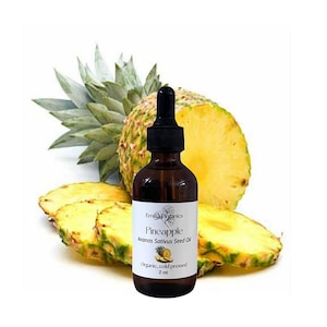 Puede incluir: Una botella de vidrio marrón con un cuentagotas negro, etiquetada como "Pineapple Ananas Sativus Seed Oil". La botella está rodeada de rodajas de piña y una piña entera. La etiqueta dice "Organic, cold pressed" y "2 oz."