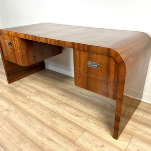 May include: A dark wood desk with curved edges and three drawers. The desk has a sleek, modern design and is made of high-quality wood.