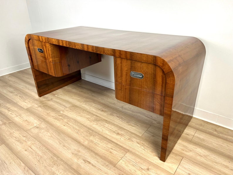 May include: A dark wood desk with curved edges and three drawers. The desk has a sleek, modern design and is made of high-quality wood.
