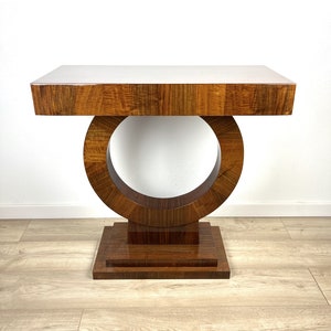 Peut inclure: Une console en bois foncé avec un plateau rectangulaire et un piétement circulaire unique. Le piétement est composé de deux cercles concentriques, le cercle intérieur étant découpé. La table a une finition polie.