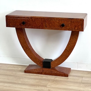 Può includere: Un tavolo consolle in legno marrone con due cassetti e una base curva. Il tavolo ha maniglie dei cassetti nere e un accento nero sulla base.
