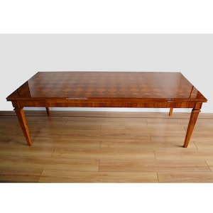 Könnte beinhalten: Ein rechteckiger Esstisch aus Holz mit einem Schachbrettmuster auf der Tischplatte. Der Tisch hat vier Beine und eine hellbraune Oberfläche.