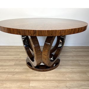 Könnte beinhalten: Ein runder Esstisch aus Holz mit einem einzigartigen, modernen Design. Die Tischplatte ist aus dunkelbraunem Holz mit glänzender Oberfläche. Das Gestell besteht aus zwei ineinandergreifenden Holzringen mit polierter Chromoberfläche.