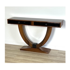 Op de afbeelding: Een console in mid-century modern stijl met een donkerbruin blad en twee zwarte lades. De tafel heeft een gebogen houten basis en een zwart accentstuk. De tafel is ongeveer 152 cm lang.