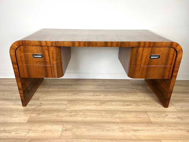 May include: A vintage wooden desk with a curved design and two drawers. The desk has a dark brown finish and silver hardware.