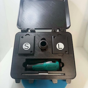 May include: Black toolbox with an open lid, containing a green and black screwdriver, and a small metal tool. The toolbox has compartments labeled "S" and "L". A blue circular object is visible at the bottom.