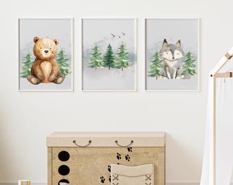 May include: Three framed watercolour prints depicting forest animals. The first print shows a brown bear, the second shows evergreen trees and birds, and the third shows a grey wolf. The prints are displayed above a wooden toy chest.