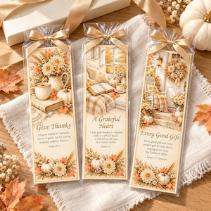 Könnte beinhalten: Drei rechteckige Lesezeichen aus Papier in durchsichtigen Kunststoffhüllen mit goldenen Schleifen. Jedes zeigt herbstliche Illustrationen von Kürbissen, Blumen und gemütlichen Szenen mit aufgedruckten Bibelversen.