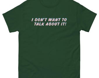 May include: Dark green t-shirt with the text "I DON'T WANT TO TALK ABOUT IT!" in a white and pink font. The shirt has short sleeves and a crew neck. The text is centered on the front of the shirt.