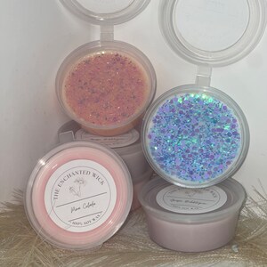 May include: Several scented wax melts in clear plastic containers. The melts are in shades of pink, peach, and lavender, with glitter. Labels read "The Enchanted Wick" and feature scent names such as "Pina Colada" and "Grape Bubblegum".