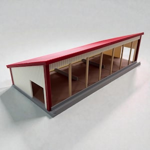 Op de afbeelding: Een miniatuurmodel van een gebouw met een rood dak, witte gevelbekleding en een grijze basis. Het gebouw heeft een open ontwerp met houten steunbalken en een bruin interieur. Het model heeft een kleine deuropening aan één kant.