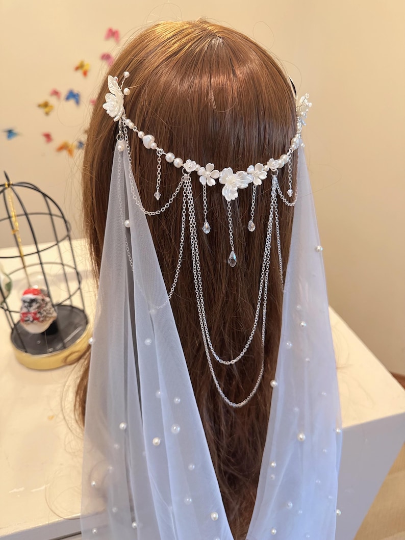 K&ouml;nnte beinhalten: Ein wei&szlig;er Braut Schleier mit Perlen Akzenten und einem silbernen Ketten Kopfschmuck verziert mit wei&szlig;en Blumen und Kristall Tropfen.