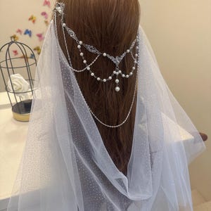 以下が含まれることがあります： 繊細なドット柄の白いブライダルベールと、シルバーチェーンとパール製のヘアピース