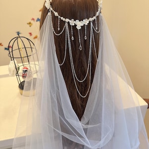 K&ouml;nnte beinhalten: Ein wei&szlig;er Braut Schleier mit einer silbernen Kette und Blumenschmuck. Die Kette hat kleine Kristalltropfen, die von ihr herabh&auml;ngen.