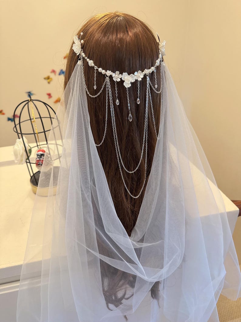 K&ouml;nnte beinhalten: Ein wei&szlig;er Braut Schleier mit einer silbernen Kette und Blumenschmuck. Die Kette hat kleine Kristalltropfen, die von ihr herabh&auml;ngen.