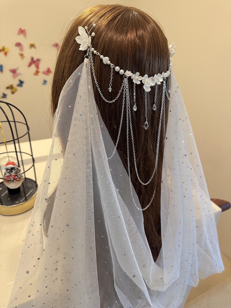 K&ouml;nnte beinhalten: Wei&szlig;er Braut Schleier mit einem zarten Blumen- und Schmetterlings Haarschmuck mit einer silbernen Kette und Perlen Akzenten.