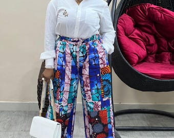 Puede incluir: Una camisa blanca abotonada combinada con pantalones de pernera ancha estampados en azul, turquesa y naranja. Un bolso blanco con una correa de cadena dorada y zapatillas deportivas en blanco y negro completan el conjunto. Los pantalones presentan un diseño de patchwork único.
