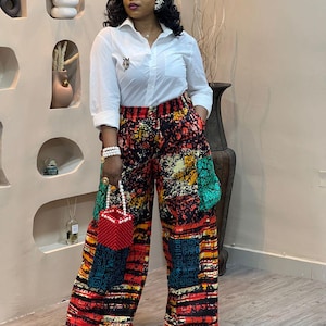 Puede incluir: Una mujer con una camisa blanca de botones y pantalones de estampado colorido. Lleva un bolso de cuentas rojas.
