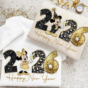 以下が含まれることがあります： 白とクリーム色のスウェットシャツに「Happy New Year 2026」のデザイン。ミッキーとミニーマウス、シャンパングラス、金と黒のグリッター数字が特徴です。背景には金色の紙吹雪とパーティーホーンがあります。