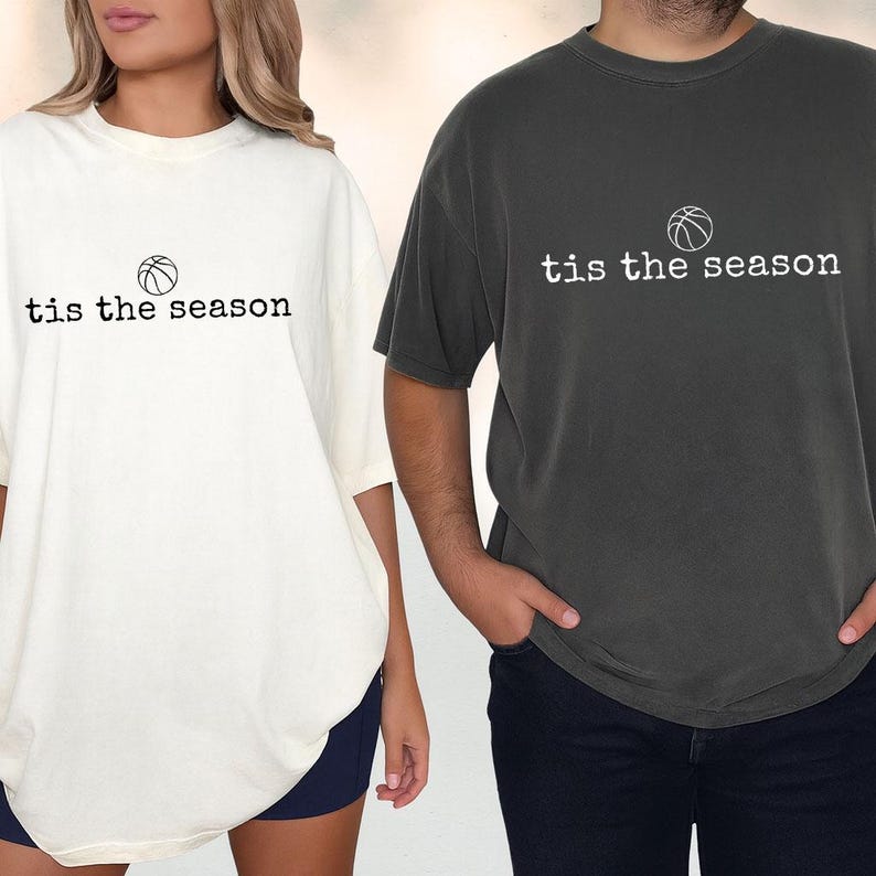 Puede incluir: Dos camisetas de gran tama&ntilde;o, una crema y otra gris carb&oacute;n, cada una con el texto "tis the season" sobre un gr&aacute;fico de baloncesto. Las camisetas est&aacute;n hechas de un material suave y tienen un corte holgado.
