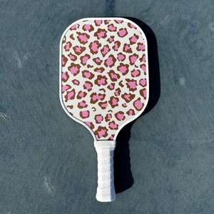 May include: A white pickleball paddle with a pink and brown leopard print design.