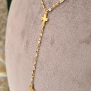 Peut inclure: Un collier en cha&icirc;ne dor&eacute;e avec des perles blanches et deux pendentifs en forme de croix dor&eacute;s.