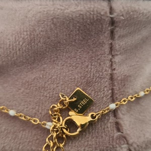 Peut inclure: Un collier en cha&icirc;ne dor&eacute;e avec de petites perles blanches et un fermoir &agrave; ressort. Le fermoir porte une petite &eacute;tiquette indiquant "S.STEEL".