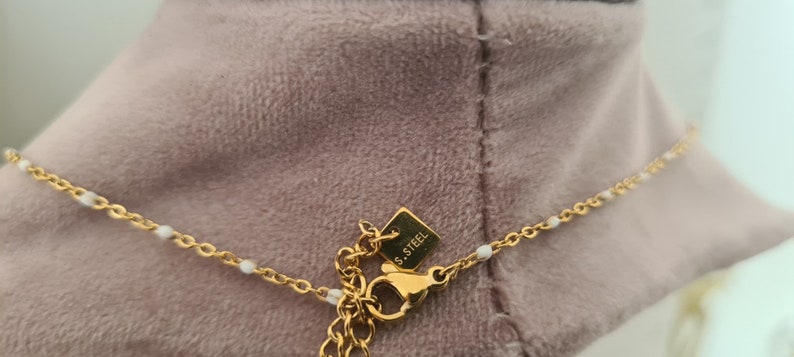 Peut inclure: Un collier en cha&icirc;ne dor&eacute;e avec de petites perles blanches et un fermoir &agrave; ressort. Le fermoir porte une petite &eacute;tiquette indiquant "S.STEEL".