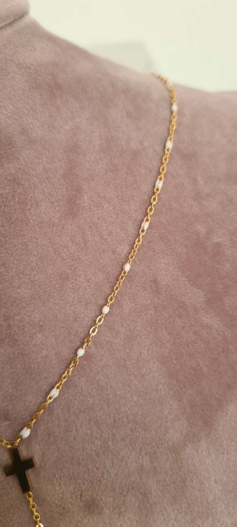 Peut inclure: Un collier en cha&icirc;ne dor&eacute;e avec un petit pendentif en forme de croix. La cha&icirc;ne est parsem&eacute;e de petites perles blanches.