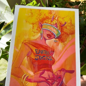 May include: A digital illustration of a person with orange hair wearing a red shirt with the text "Earth Sucks" in blue. The person is wearing a futuristic visor and has a pink skin tone.
