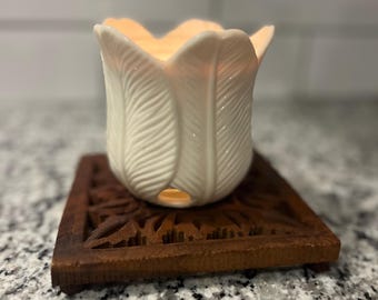 May include: A white ceramic candle holder shaped like a flower with a carved wooden coaster. The candle holder has a textured surface with a leaf design.