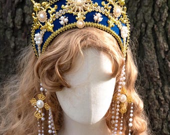 Op de afbeelding: Een koningsblauwe en gouden kroon met parelaccenten en gouden punten. De kroon wordt gecombineerd met bijpassende gouden oorbellen en een gelaagde parelketting. De sieraden worden getoond op een mannequinhoofd met blond haar.