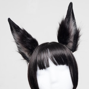 May include: Black and gray faux fur fox ears attached to a black wig. The ears are upright and pointed, with a fluffy texture. The wig has straight, black bangs and a bob cut. The ears are a popular accessory for cosplay or costume parties.