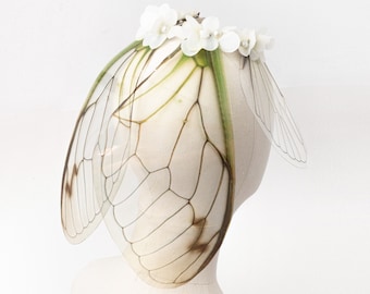 May include: A white headband with white flower accents and a pair of translucent wings with brown and green veins.