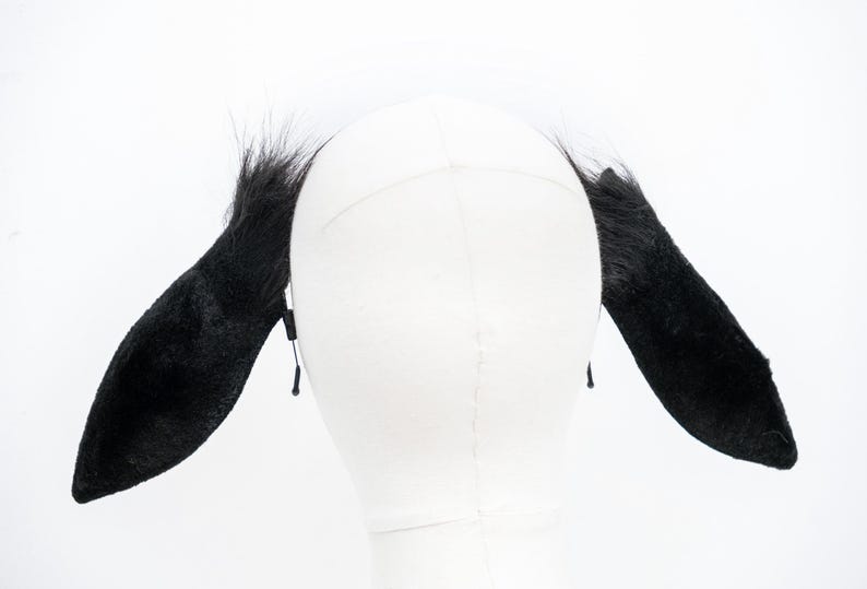 May include: Black furry animal ears headband. The headband is made of black faux fur and has two long, floppy ears. The ears are attached to a black elastic headband.