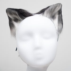 May include: A pair of black and white faux fur cat ears headband. The headband is made of black elastic and the ears are made of soft, fluffy fur.