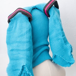 May include: A blue knitted hat with two long, frayed ear flaps and black and pink elastic bands.