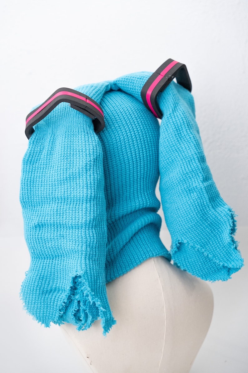 May include: A blue knitted hat with two long, frayed ear flaps and black and pink elastic bands.
