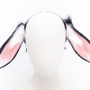 May include: A pair of black and white bunny ears headband with pink fur on the inside of the ears.