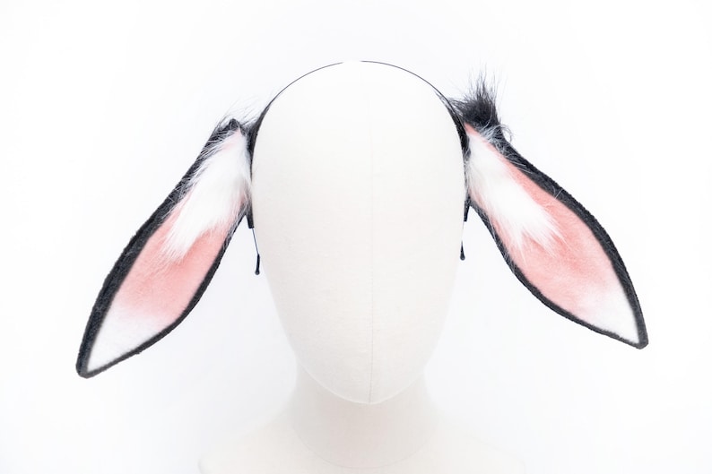 May include: A pair of black and white bunny ears headband with pink fur on the inside of the ears.