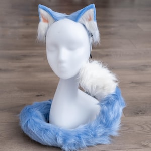 May include: A blue and white faux fur cat tail and headband set. The headband has cat ears with white fur on the inside of the ears. The tail is long and fluffy with a white tip.