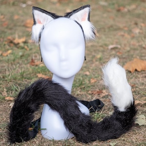May include: Black and white cat ears headband with a fluffy white tail. The headband is on a white mannequin head and the tail is lying on the ground.