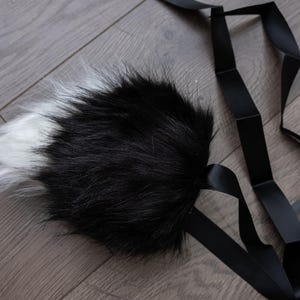 May include: A black and white faux fur tail with a black ribbon attached.